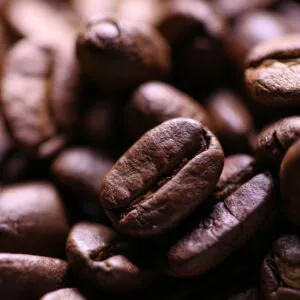 Close-up of a shiny, roasted Yemeni coffee bean surrounded by other coffee beans.